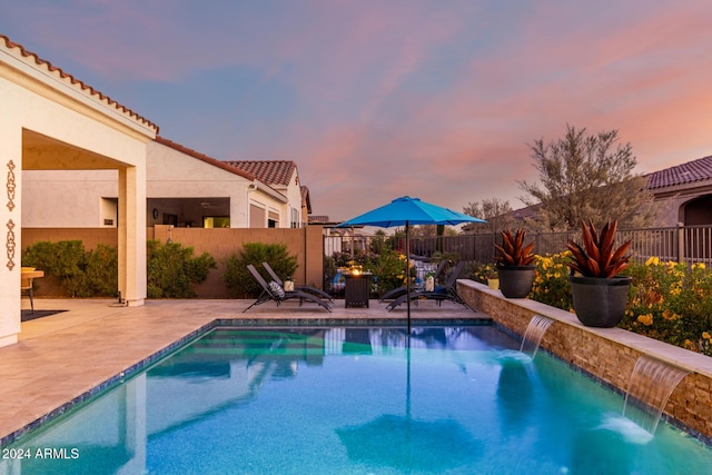 pool at dusk featuring pool water feature and a patio area