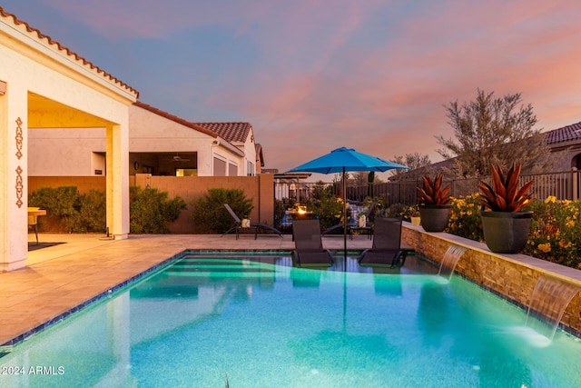 pool at dusk featuring pool water feature and a patio