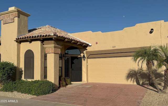 view of front of home featuring stucco siding, driveway, a tile roof, and a garage