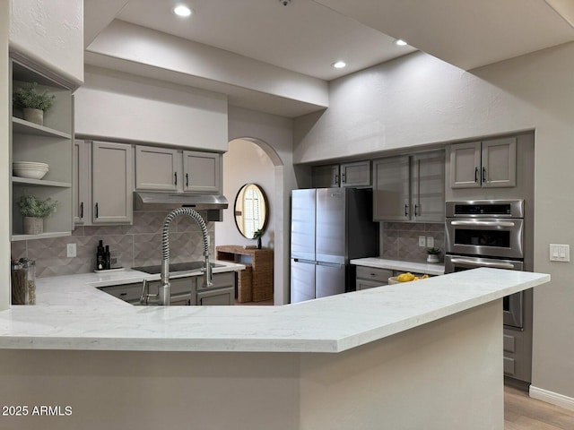 kitchen with open shelves, stainless steel appliances, arched walkways, and gray cabinets