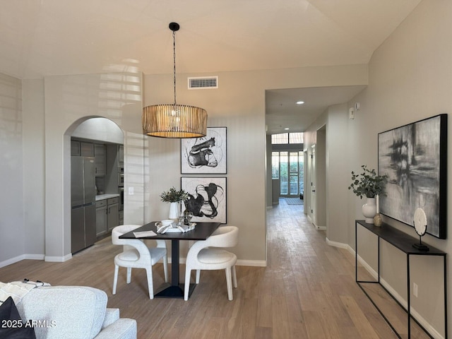 dining space with baseboards, arched walkways, visible vents, and light wood-type flooring