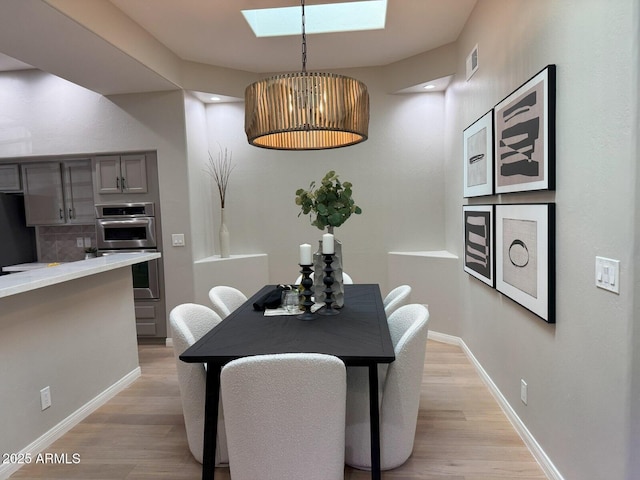 dining area featuring light wood finished floors, a skylight, and baseboards