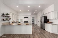 kitchen with a peninsula, dark wood-type flooring, freestanding refrigerator, and white cabinets