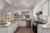 kitchen with dark wood finished floors, light stone counters, a peninsula, stainless steel appliances, and wall chimney range hood