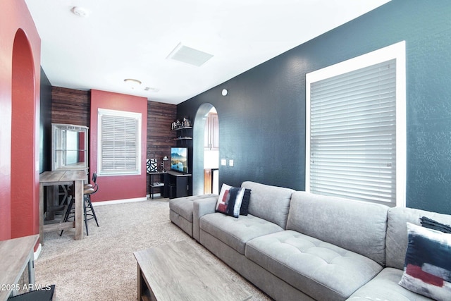 carpeted living room with arched walkways, baseboards, and a textured wall