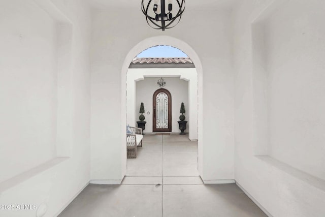 corridor with arched walkways, tile patterned flooring, and an inviting chandelier