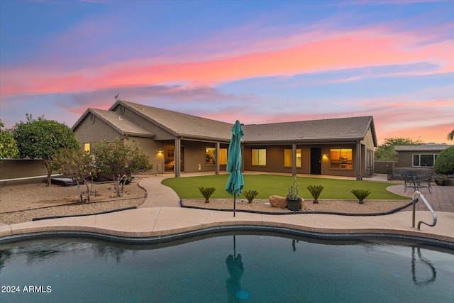 back house at dusk featuring a yard and a patio