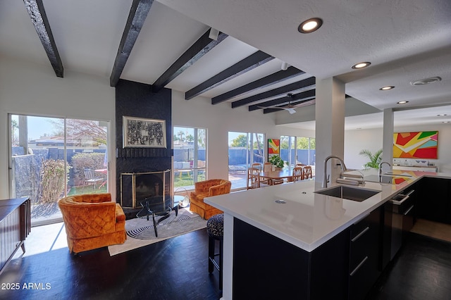 kitchen with dark wood-type flooring, a kitchen bar, sink, beam ceiling, and a fireplace