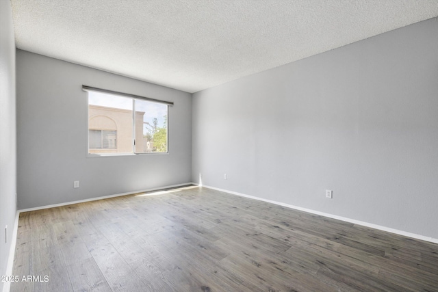 unfurnished room with baseboards, a textured ceiling, and wood finished floors
