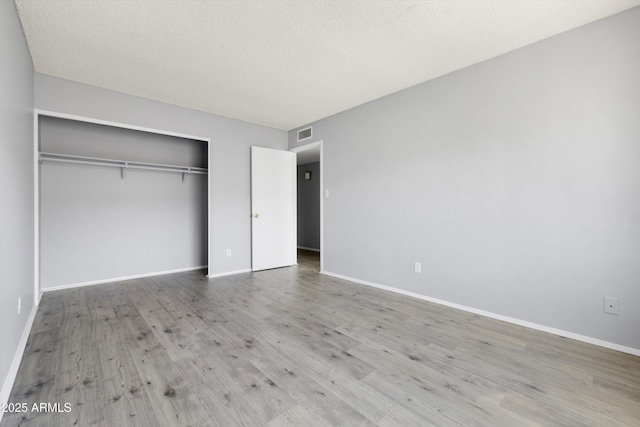 unfurnished bedroom with baseboards, a closet, wood finished floors, and visible vents