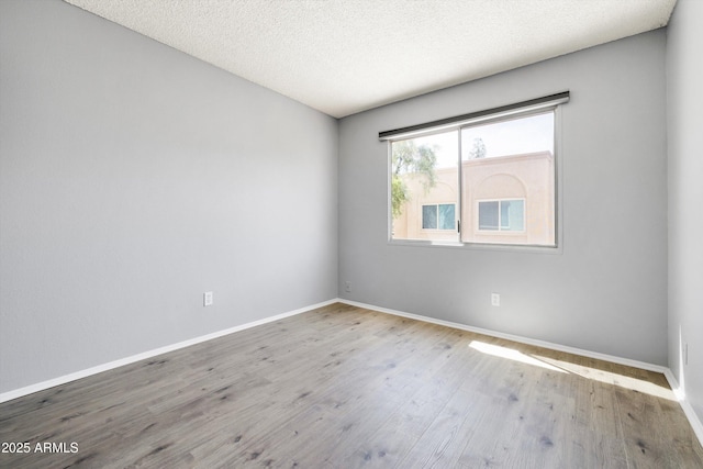 spare room featuring baseboards, a textured ceiling, and wood finished floors
