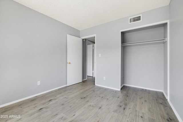 unfurnished bedroom with baseboards, a closet, wood finished floors, and visible vents