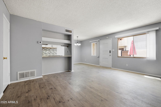 unfurnished living room featuring visible vents, a textured ceiling, wood finished floors, and a notable chandelier