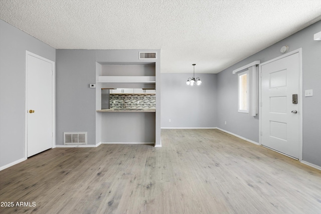unfurnished living room with wood finished floors, a textured ceiling, a chandelier, and visible vents