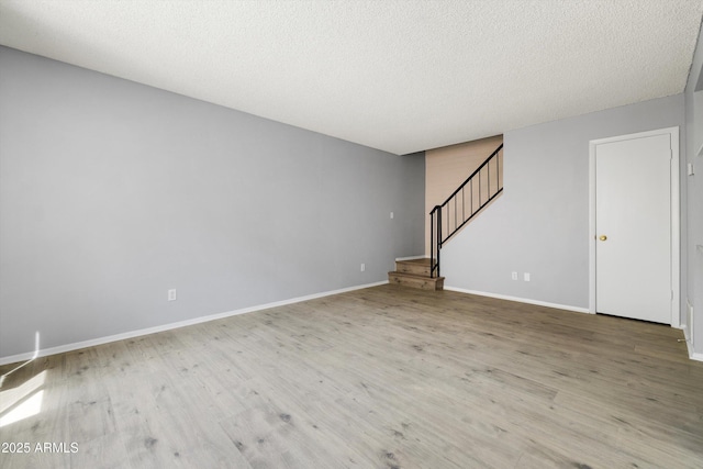 unfurnished living room with stairs, a textured ceiling, baseboards, and wood finished floors