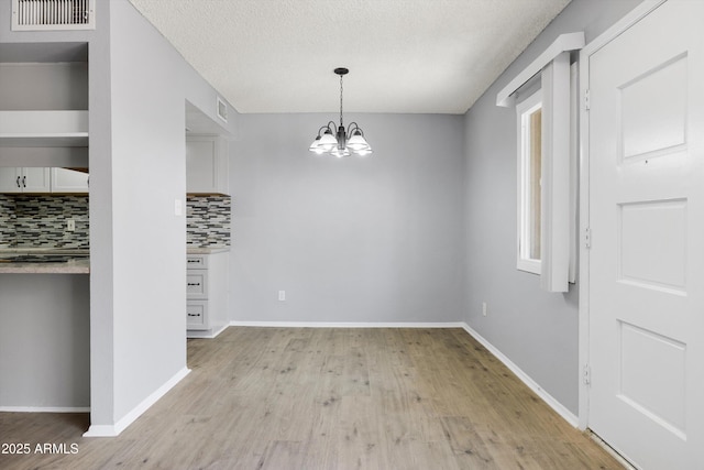 unfurnished dining area featuring visible vents, light wood-style floors, baseboards, a textured ceiling, and a chandelier