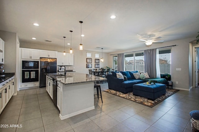 kitchen featuring pendant lighting, a center island with sink, open floor plan, a sink, and black appliances