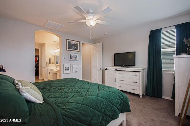 carpeted bedroom featuring a ceiling fan, arched walkways, visible vents, and ensuite bath