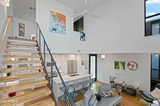 staircase with a towering ceiling, wood-type flooring, sink, and ceiling fan