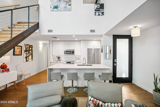 kitchen with sink, a center island with sink, white cabinetry, stainless steel appliances, and light wood-type flooring