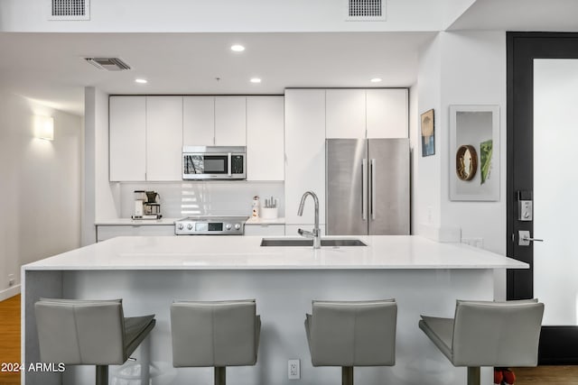 kitchen with stainless steel appliances, sink, kitchen peninsula, white cabinetry, and a kitchen bar