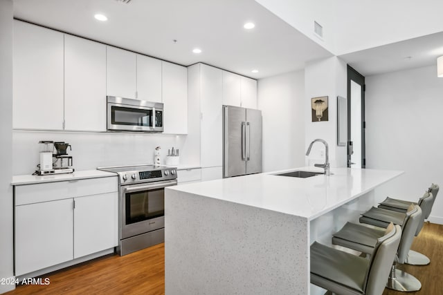 kitchen featuring a kitchen island with sink, light hardwood / wood-style flooring, sink, stainless steel appliances, and white cabinetry