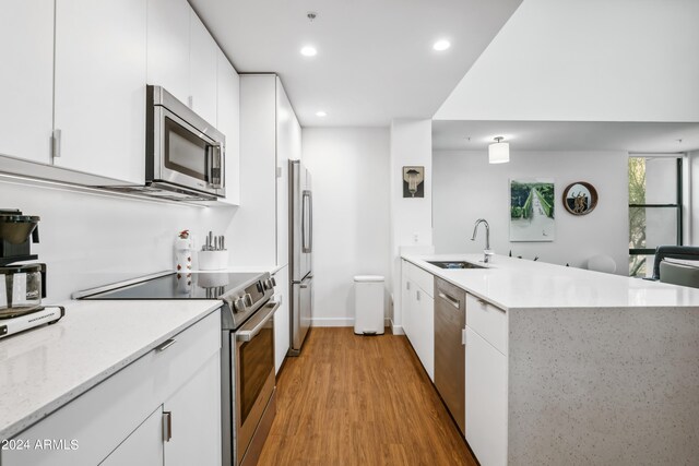 kitchen with white cabinets, sink, kitchen peninsula, appliances with stainless steel finishes, and light wood-type flooring