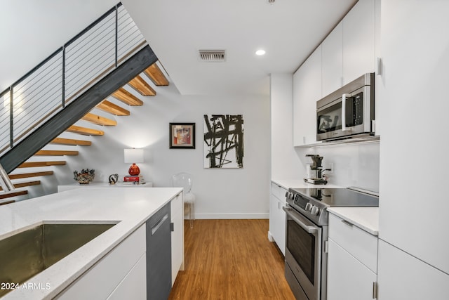 kitchen with white cabinets, stainless steel appliances, sink, and light hardwood / wood-style flooring