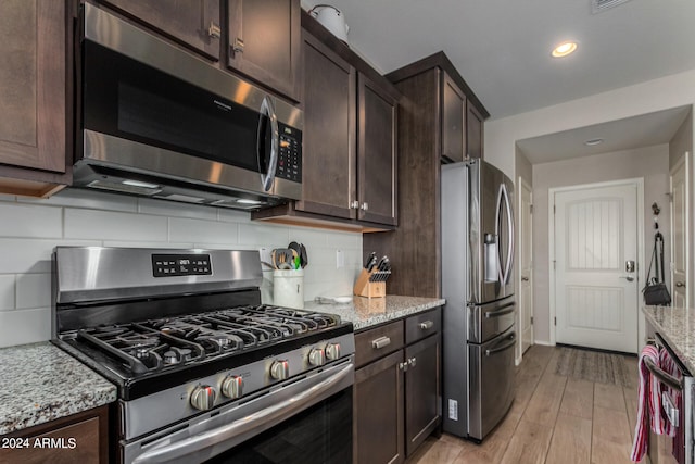 kitchen featuring tasteful backsplash, light stone counters, appliances with stainless steel finishes, and dark brown cabinetry