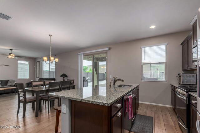 kitchen featuring tasteful backsplash, light stone counters, a center island with sink, appliances with stainless steel finishes, and light hardwood / wood-style flooring