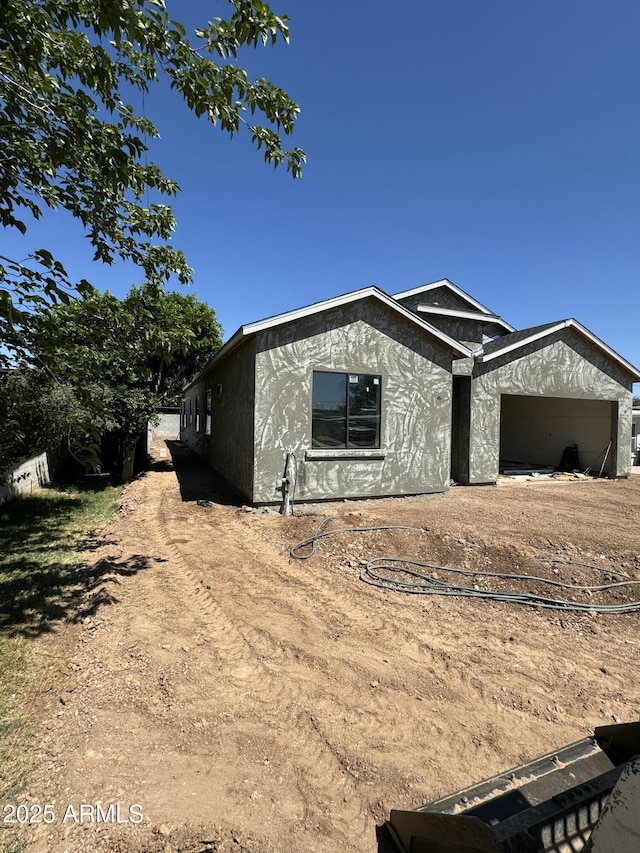 view of front of house with a garage, dirt driveway, and stucco siding