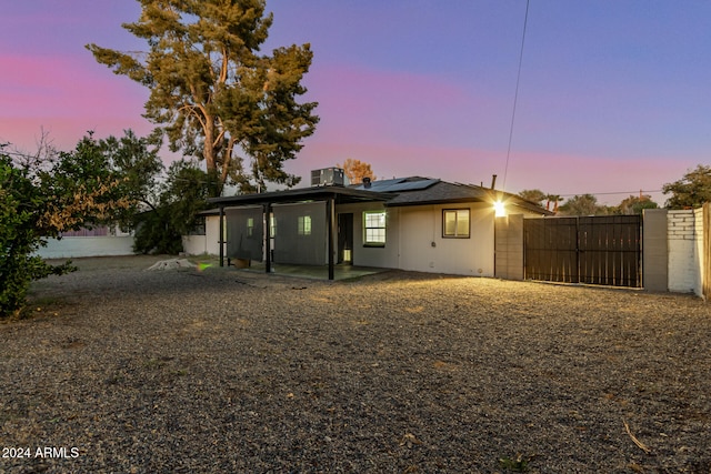 back house at dusk featuring a patio, solar panels, and cooling unit