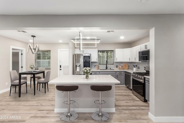 kitchen with stainless steel appliances, sink, decorative light fixtures, and light hardwood / wood-style flooring