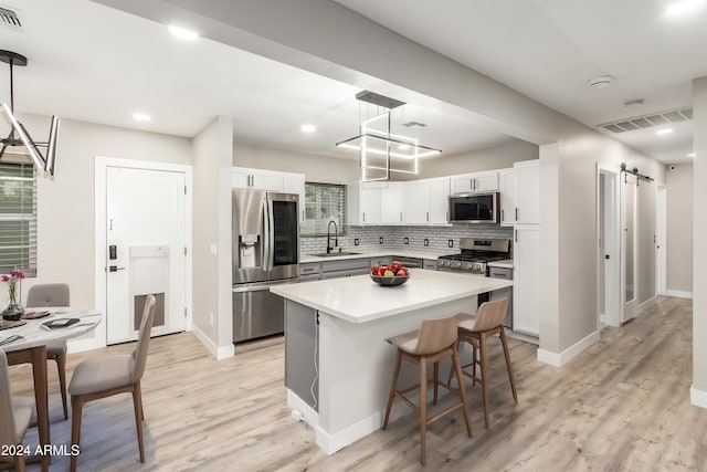 kitchen featuring appliances with stainless steel finishes, decorative light fixtures, white cabinets, a kitchen island, and a barn door