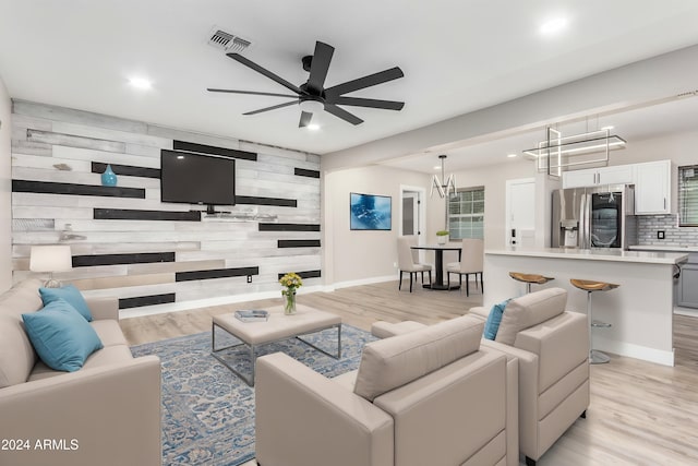 living room featuring light wood-type flooring, ceiling fan with notable chandelier, and wooden walls