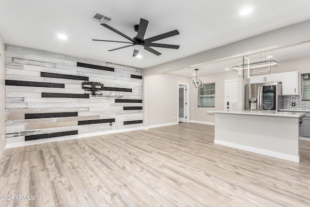 unfurnished living room featuring ceiling fan with notable chandelier, wooden walls, and light wood-type flooring