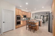14687 W Amelia Ave, Goodyear, AZ 85395 - kitchen featuring stainless steel double oven, a kitchen breakfast bar, recessed lighting, light brown cabinets, and a kitchen island