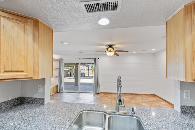 kitchen featuring visible vents, light brown cabinets, a textured ceiling, and a sink