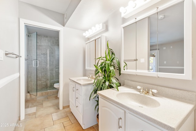 bathroom featuring toilet, two vanities, a stall shower, and a sink