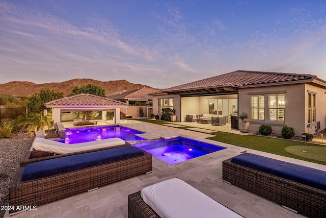 pool at dusk with an in ground hot tub, an outdoor hangout area, a mountain view, a gazebo, and a patio