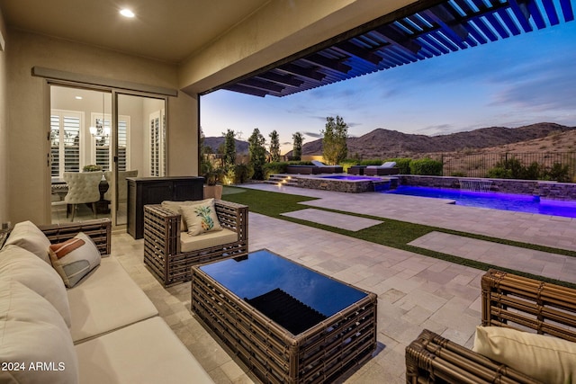 patio terrace at dusk featuring a mountain view, a pool with hot tub, outdoor lounge area, and pool water feature