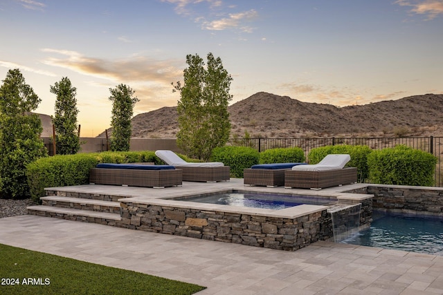 pool at dusk featuring outdoor lounge area, pool water feature, a mountain view, and a patio area