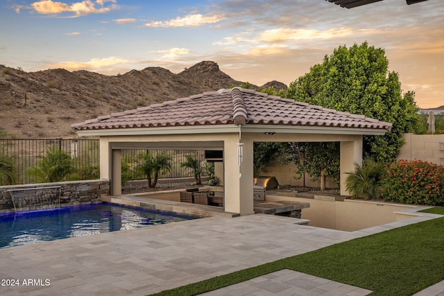 pool at dusk with a grill, a mountain view, pool water feature, a gazebo, and a patio area