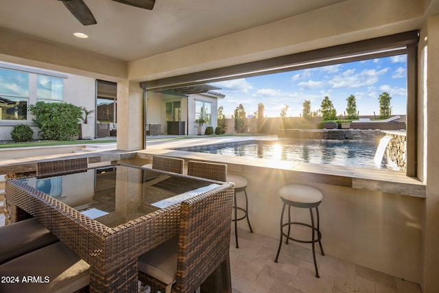 view of swimming pool featuring exterior bar, a water view, pool water feature, a patio, and ceiling fan