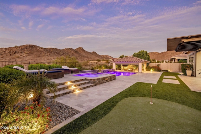 pool at dusk featuring a gazebo, an in ground hot tub, a mountain view, and a patio area