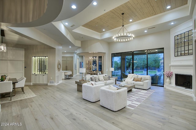 living room with a towering ceiling, a tray ceiling, an inviting chandelier, wooden ceiling, and light hardwood / wood-style floors