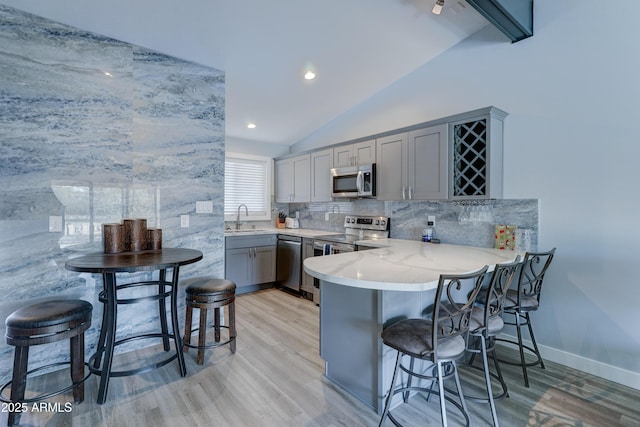 kitchen featuring sink, gray cabinetry, a kitchen bar, kitchen peninsula, and stainless steel appliances