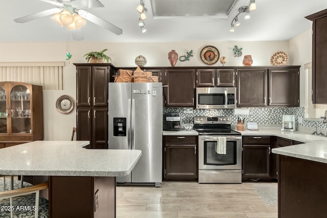 kitchen with dark brown cabinetry, a breakfast bar area, tasteful backsplash, ceiling fan, and stainless steel appliances