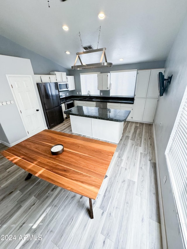 kitchen with stainless steel appliances, vaulted ceiling, a center island, light hardwood / wood-style floors, and white cabinetry