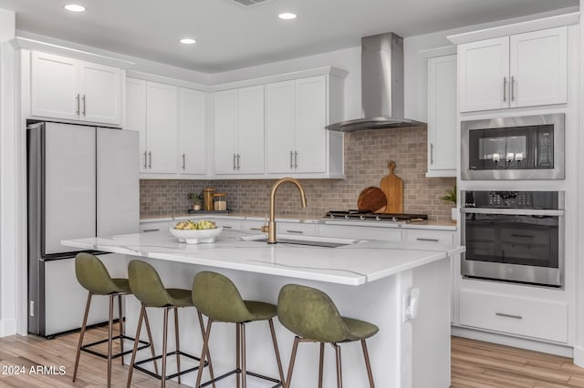 kitchen with white cabinetry, light wood-type flooring, sink, wall chimney exhaust hood, and stainless steel appliances